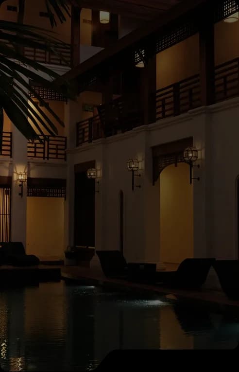 Hotel courtyard with a pool at night, lit by wall lanterns